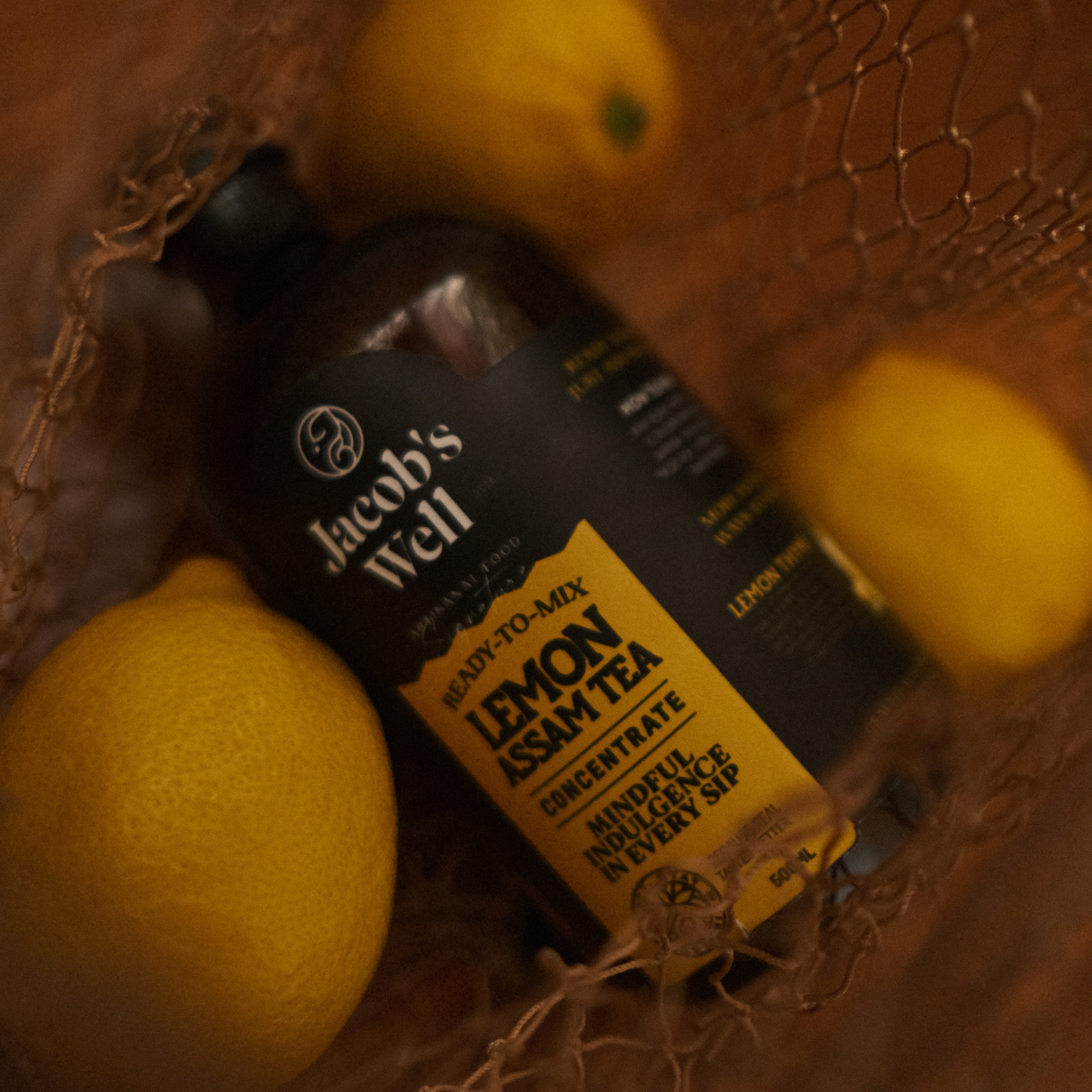Close up of a bottle of Jacob's Well Lemon and Kumquat Fruit Tea Concentrate surrounded by lemons.
